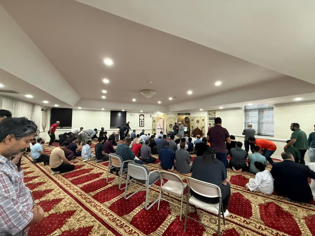 Worshippers in the prayer hall on the red and gold carpet, with the Imam at the front by the mihrab